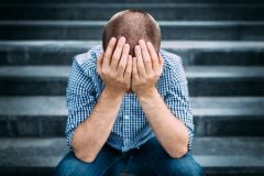 Sad Man Covering his Face with Hands Sitting on Stairs.