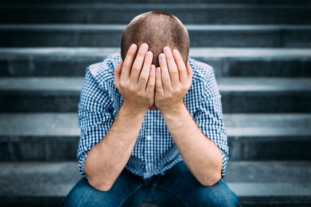 Sad Man Covering his Face with Hands Sitting on Stairs.
