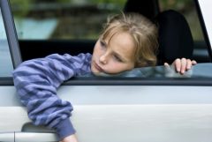 A little girl in a car is hanging out the window.