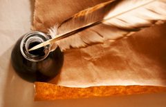 Feather and ink bottle on a sheet of paper.